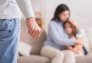 Domestic abuse. Scared woman with little daughter suffering from husband's violence, male fist in foreground, selective focus