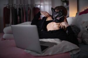 A young girl wears a cat mask as she uses her laptop.